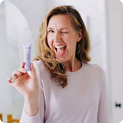 woman winking at the camera holding small tube of frownies eye cream