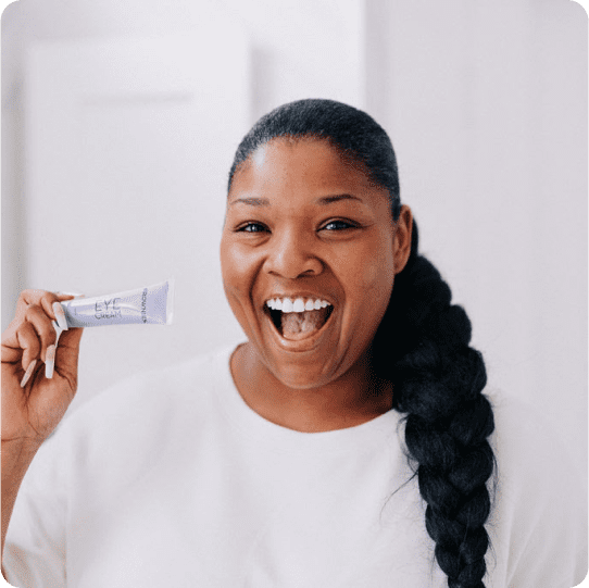 smiling woman holding a tube of under eye cream