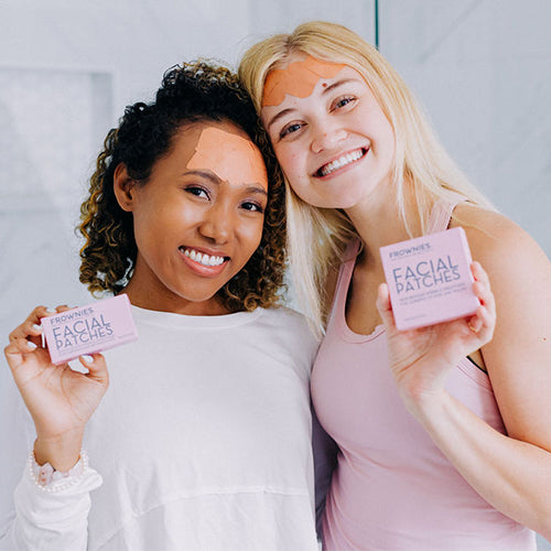 two woman smiling holding pink boxes of frownies facial patches