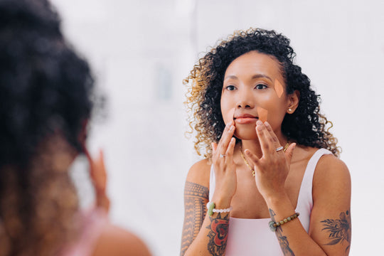 woman of color with curly hair and tattoos on arms applying frownies facial patches to the corners of the eyes and mouth