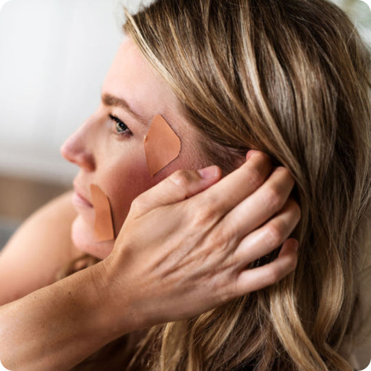 woman touching her hair wearing frownies facial patches at the corner of her eyes and mouth