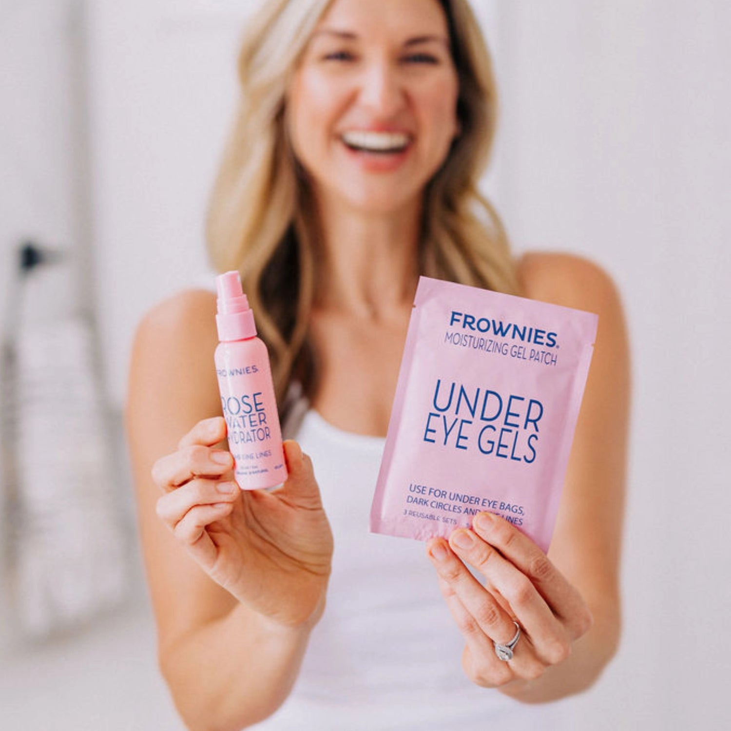A smiling woman with blonde hair holding Frownies under eye gels and rose water hydrator.