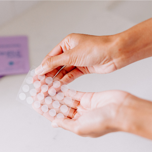 woman's hands holding sheet of transparent round pimple patch stickers