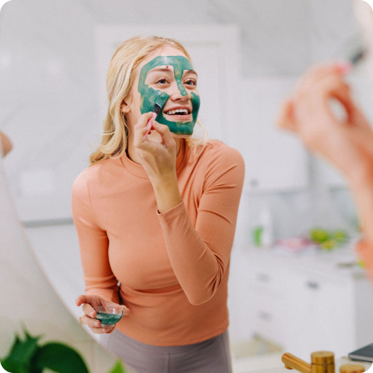 woman applying green clay mud mask to her face