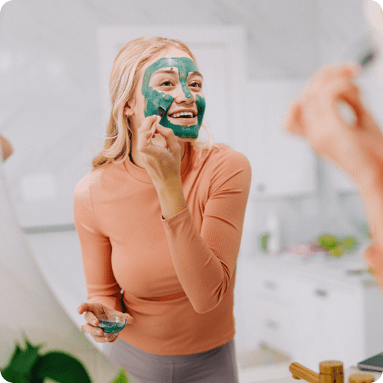 woman applying green clay mask to her face