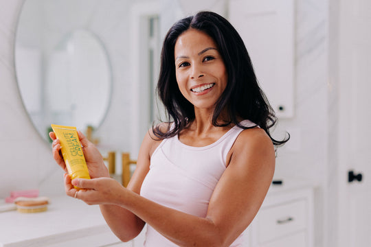 woman holding a bottle of cellulite cream smiling