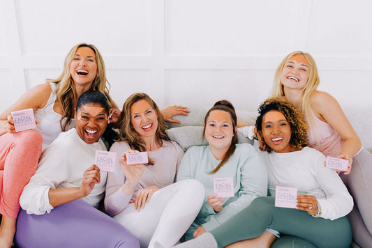 Group of six women sitting on a couch and smiling while holding boxes of Frownies Facial Patches