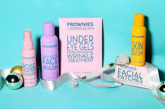 Six Frownies products including Rose Water Hydrator Spray, pH Balancing Face Wash, Under Eye Gels, Skin Serum, Facial Patches, and rose quartz facial roller on tiffany blue background with silver holiday ribbon 