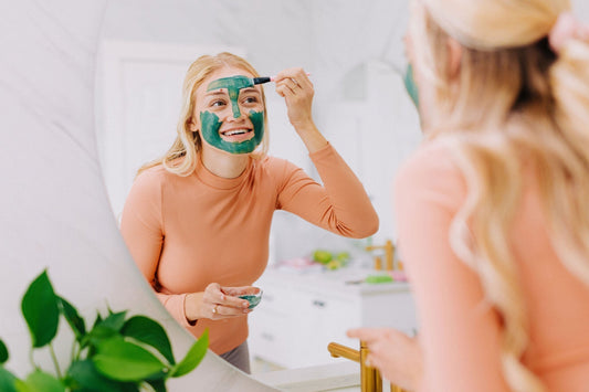 Woman applying a clay mask at the bathroom mirror