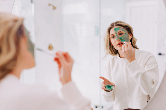 Woman applying Blue Green Algae mask to her face in the bathroom mirror