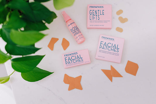 Frownies facial patches loose and in boxes on a white countertop with a plant off to the side