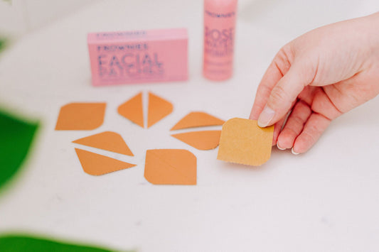 Person holding a Frownies facial patch with a box and rose water spray in the background
