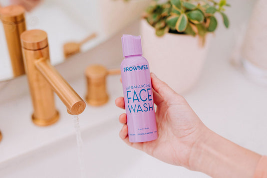 Person holding Frownies face wash over a sink with running water in the background