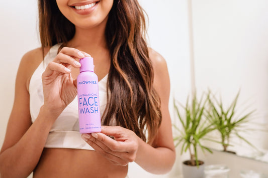 Woman in background holding out Frownies pH Balancing Face Wash purple bottle