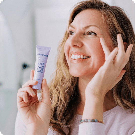 woman applying frownies eye cream holding small purple tube