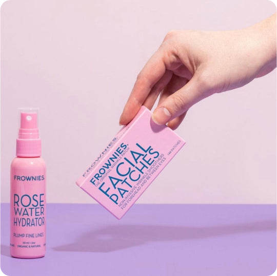 hand placing pink box of frownies facial patches with pink bottle of rose water facial toner