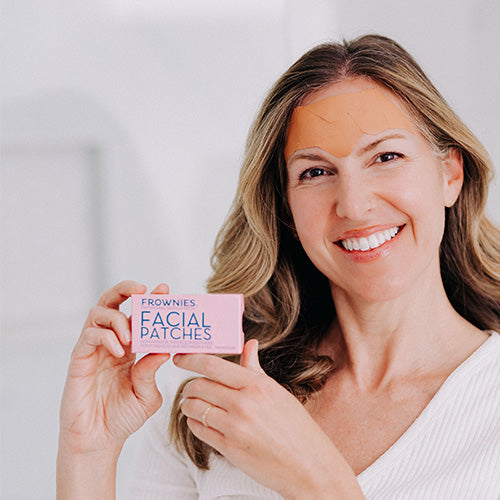 woman holding pink box of frownies wrinkle patches and wearing wrinkle patches on forehead to smooth forehead wrinkles