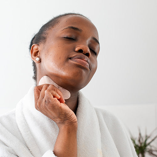 woman of color performing facial massage on neck with gua sha stone