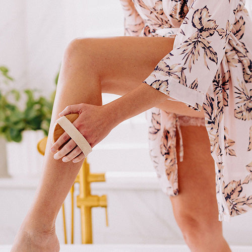 close up of woman's hand holding round body brush massaging thigh 