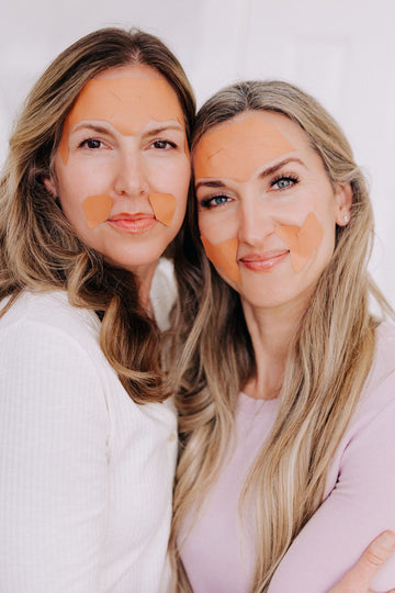 Two women with heads together wearing frownies facial patches on forehead and corners of the mouth