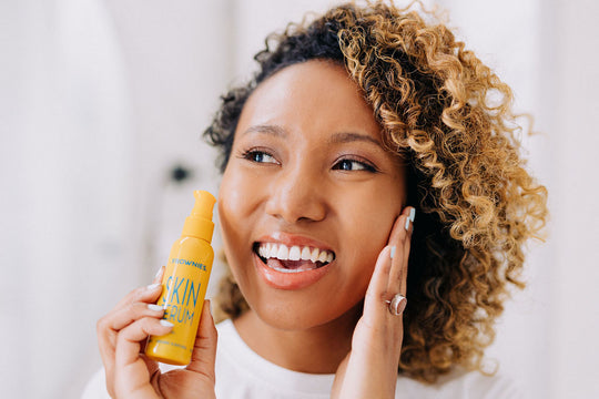 woman smiling touching her face and holding yellow bottle of frownies skin serum