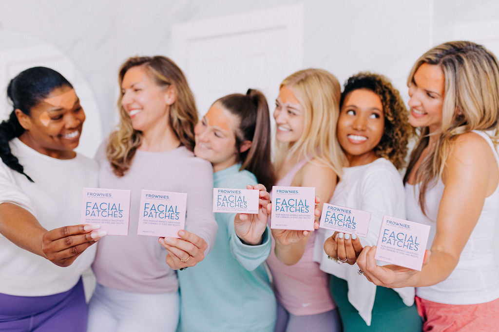 six woman in background holding out various pink boxes of frownies facial patches
