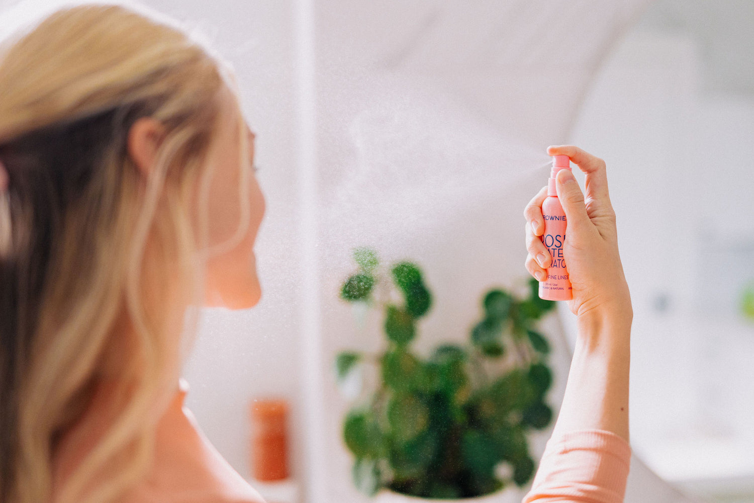 blonde woman spraying frownies rose water hydrator on face