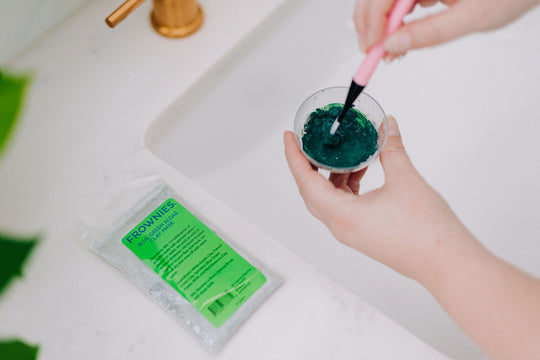 hands mixing green detoxifying clay mask in mini bowl with applicator brush