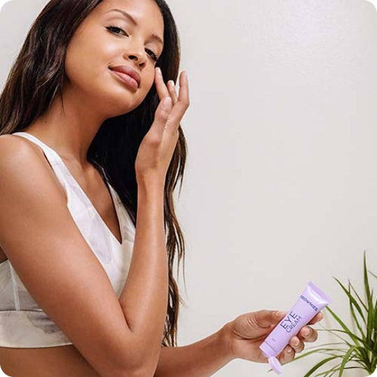 woman touching face holding purple tube of frownies eye cream