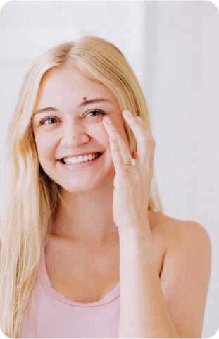young blonde woman smiling and touching face applying frownies eye cream 