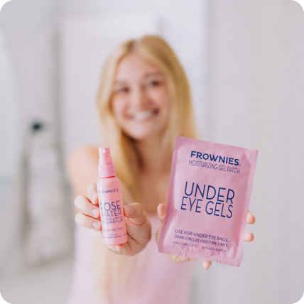 woman holding frownies rose water spray bottle and under eye gels in pink packaging to the camera