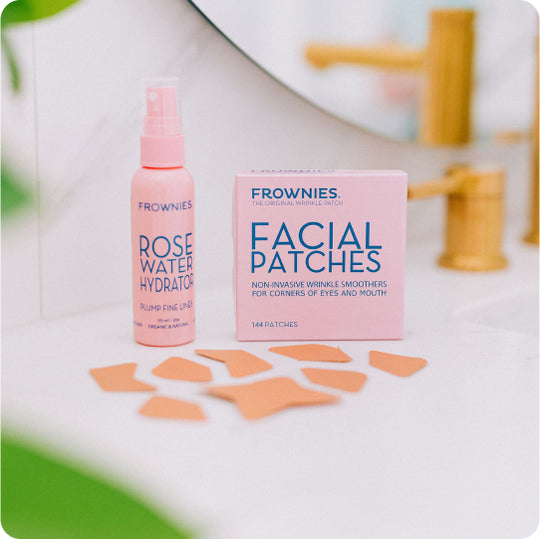 pink bottle of frownies rose water hydrator and frownies facial patches for corner of the eyes and mouth with separated brown facial patches on countertop