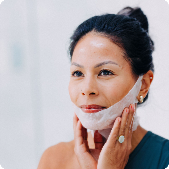 woman applying white soft cotton chin up neck mask under lower lip, over jawline and neck and over ears to smooth neck lines