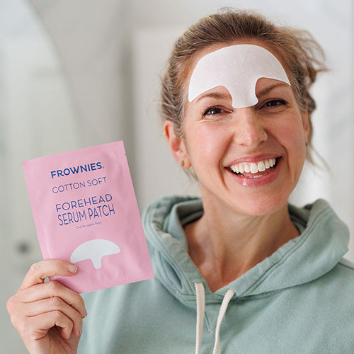 woman with frownies serum patch on her forehead holding the patch package 