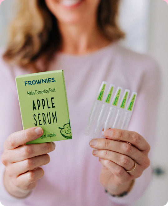woman in background holding frownies box of apple serum and multiple ampoules