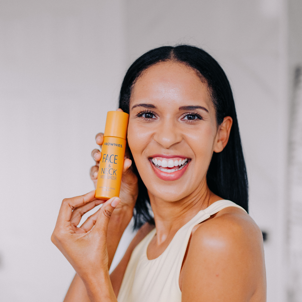 Woman holding an orange bottle of Frownies Face & Neck moisturizer with a blurred background
