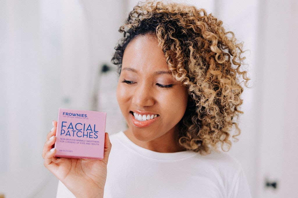 woman of color with natural hair holding pink box of frownies facial patches