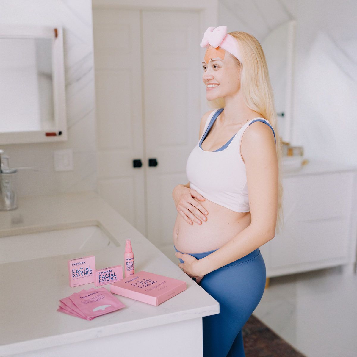 Pregnant woman standing in a bathroom with skincare products on the counter.