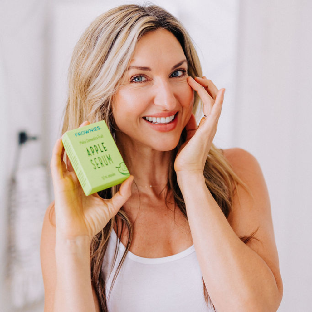 Woman smiling holding a green box labeled 'Apple Serum' in front of a white background.