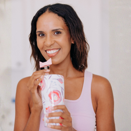Woman holding a tumbler with a straw and a Wrinkie Straw Tip, smiling against a plain background