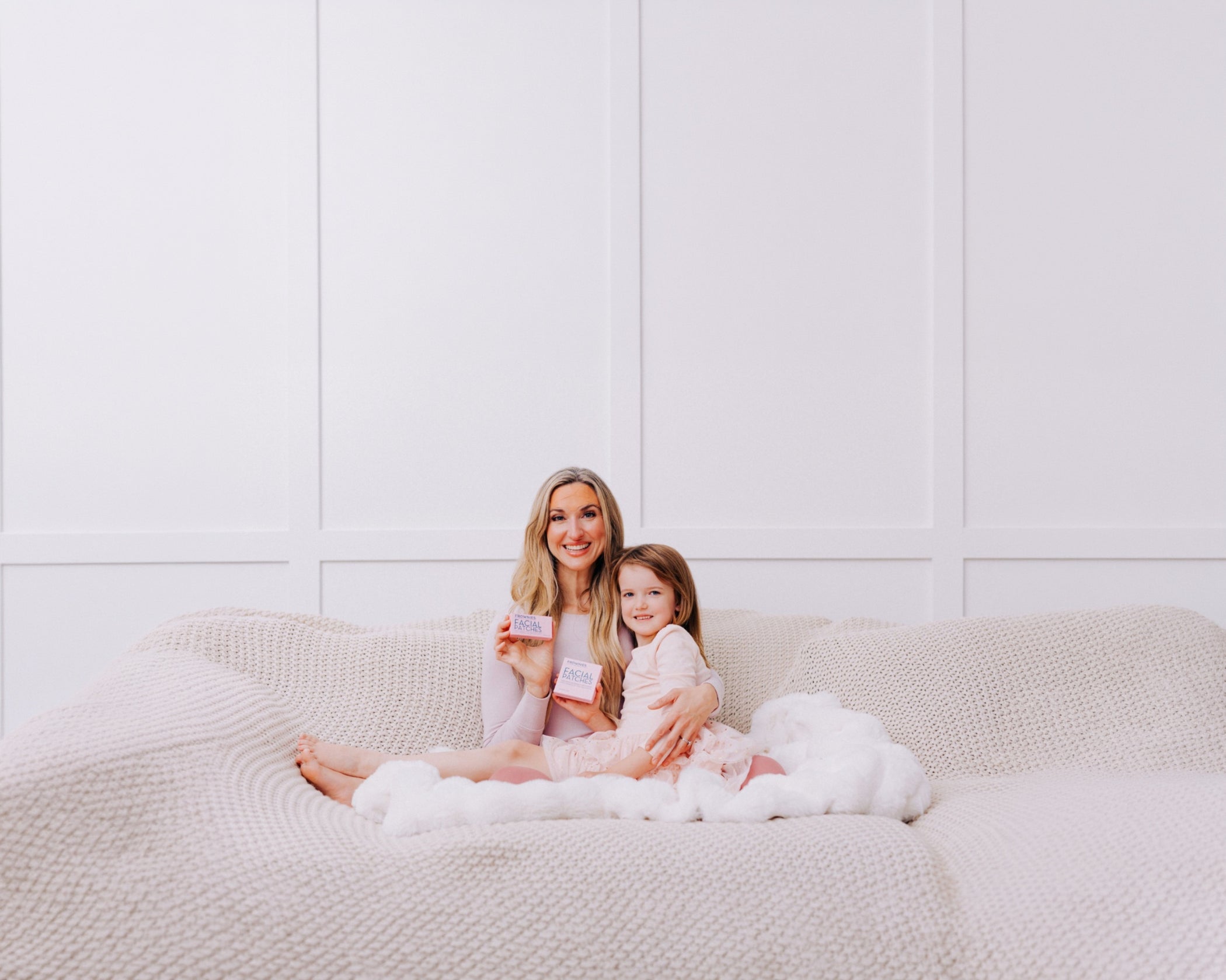 Woman and child sitting on a couch holding Frownies facial patches against a white wall