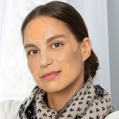 woman with hair pulled back wearing frownies facial patches on forehead, corners of the eyes, and corners of the mouth to smooth wrinkles