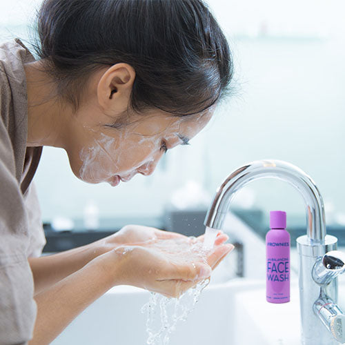 Woman washing her face  a purple bottle of Frownies pH Balancing Face Wash is on the sink 