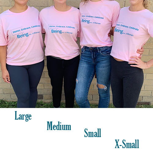 Woman wearing a pink tee with blue text that reads Honor, Embrace, Celebrate, Being...a Woman with size large medium small and x-small