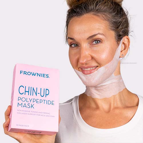 Light skinned woman holding a box of Frownies Chin -up Polypeptide Mask while wearing the mask on her chin and jawline 