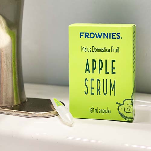 Green box sitting next to bathroom faucet of Frownies Apple Serum 15/1 ml ampoules 